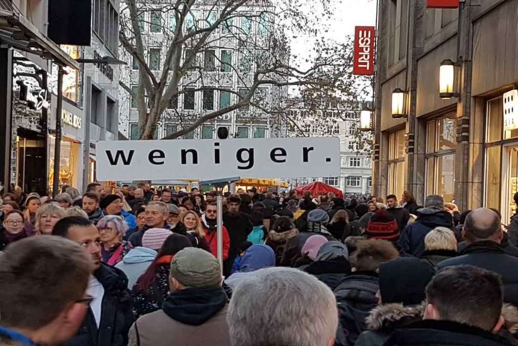 Blick in die Kölner Hohe Straße voll mit Menschen und einem Schild, auf dem "weniger." steht. © Tom Rübenach