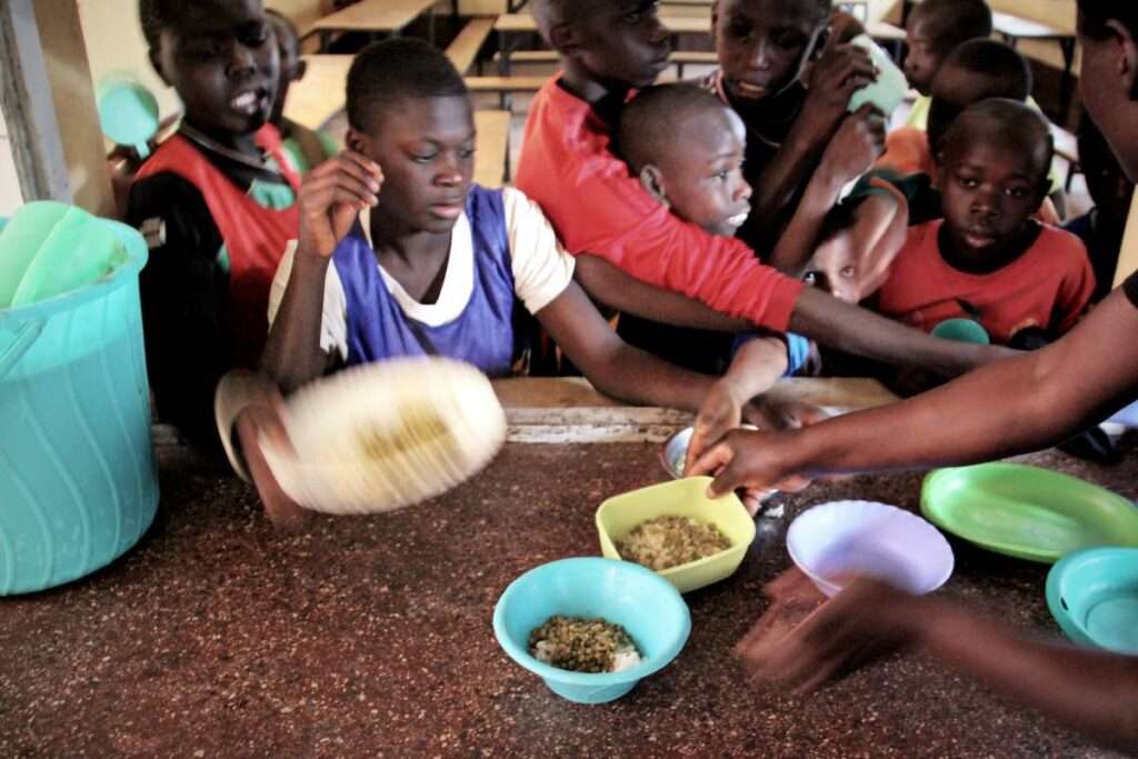 Kinder im Ayiera-Center im Slum Korogocho erhalten Mittagessen. Sie haben Plastikschüsseln mit Reis und ein paar Erbsen. | Foto © Tom Rübenach
